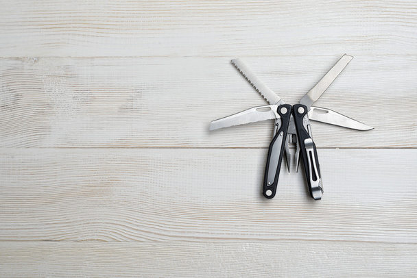 Multi tool with black handles on a white wooden background. Top view of desktop - Fotó, kép