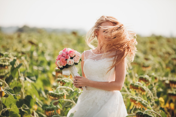 Elegant blonde bride with long hair and a bouquet of sunflowers in the field - Фото, изображение