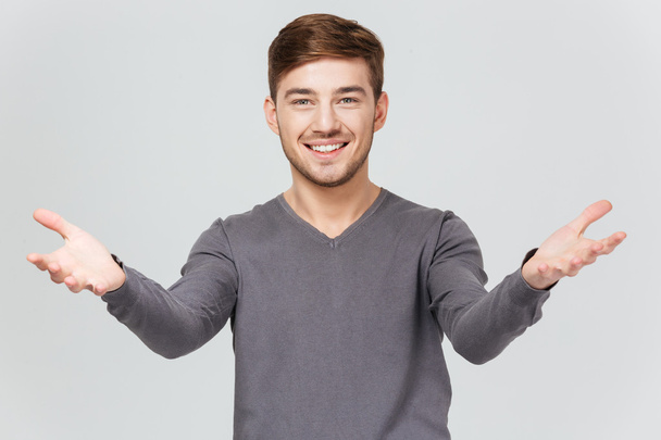 Cheerful handsome young man smiling and showing welcoming gesture  - Foto, imagen