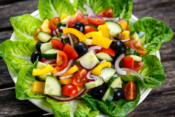 Ensalada de verduras frescas, aceitunas negras, tomates cherry, pimiento amarillo, cebolla roja, pepino. Sobre mesa de madera
 - Foto, Imagen