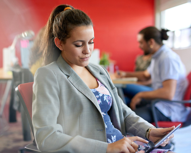 Diseñadora femenina segura trabajando en una tableta digital en un espacio de oficina rojo creativo
 - Foto, Imagen