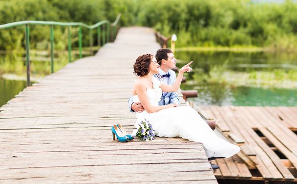 Beautiful young wedding couple sitting on the pier - Photo, Image