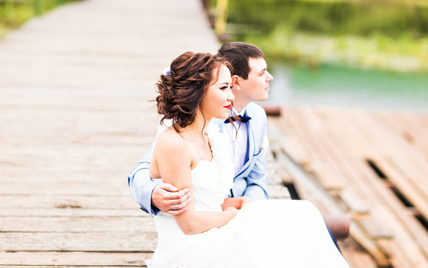 Beautiful young wedding couple sitting on the pier - Photo, Image