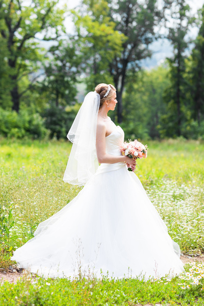 Beautiful bride with wedding bouquet of flowers outdoors in green park. - Photo, Image