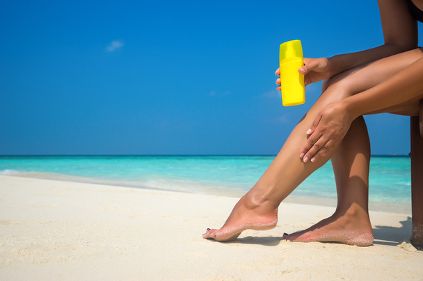 Woman applying sunblock cream on leg on beautiful tropical beach - Foto, Imagem