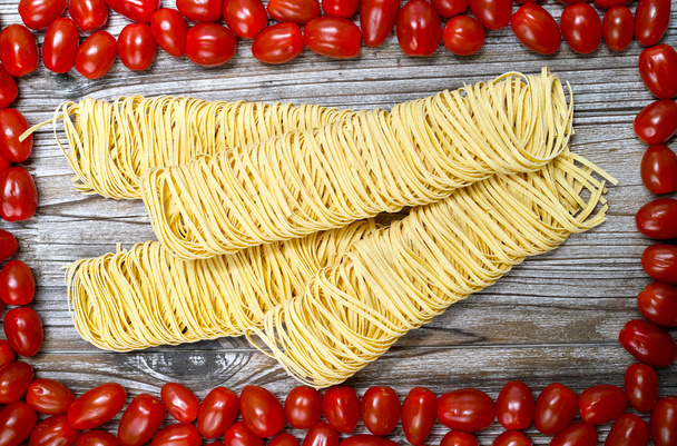 Homemade fettuccini pasta, small red tomatoes on wood - Photo, Image