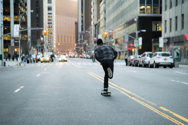 Back figure of young skateboarder cruising donw the city street  - Foto, Bild