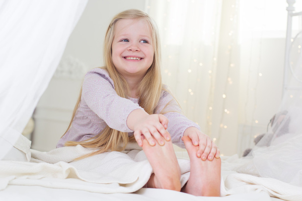 Happy child girl is sitting in the bed, good morning - Фото, изображение