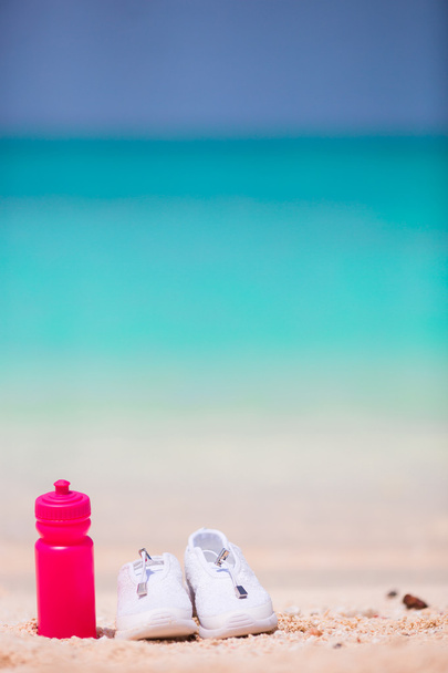 Sport cipő és egy üveg fehér homokos strandon - Fotó, kép