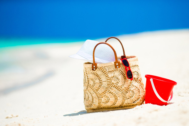 Acessórios de praia - saco de palha, chapéu branco e óculos de sol vermelhos na praia
 - Foto, Imagem