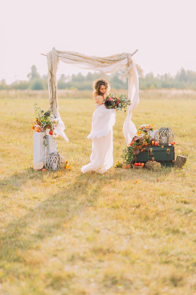 Charming bride standing on field with wedding arch at background - Fotoğraf, Görsel