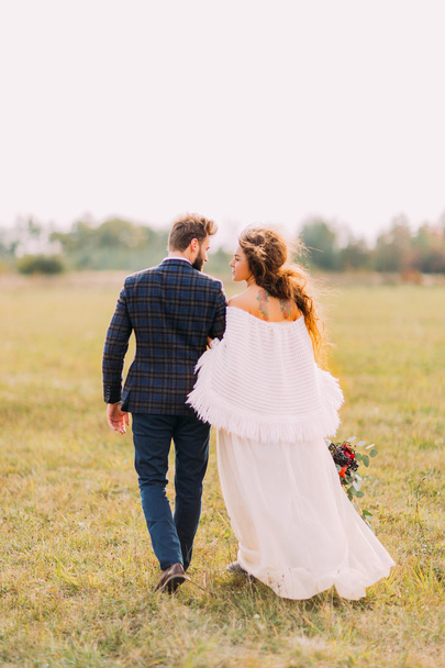 Happy bride and groom walking on the field at countryside - Photo, image