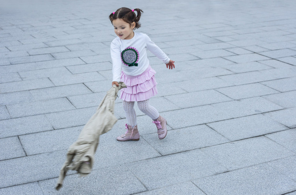 Счастливая трехлетняя девочка играла со своим пальто в городе
 - Фото, изображение