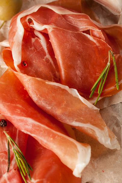 closeup of thin slices of prosciutto with mixed olives and paprika on wooden cutting board - Photo, image