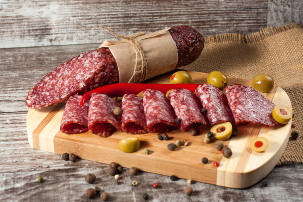 Italian salami with olives and spices on wooden background - Photo, Image