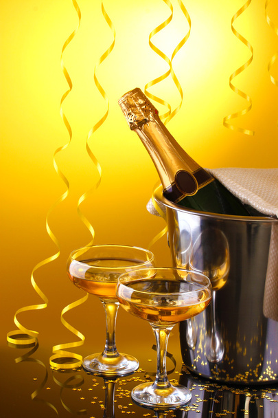 Champagne bottle in bucket with ice and glasses of champagne, on yellow background - Foto, immagini