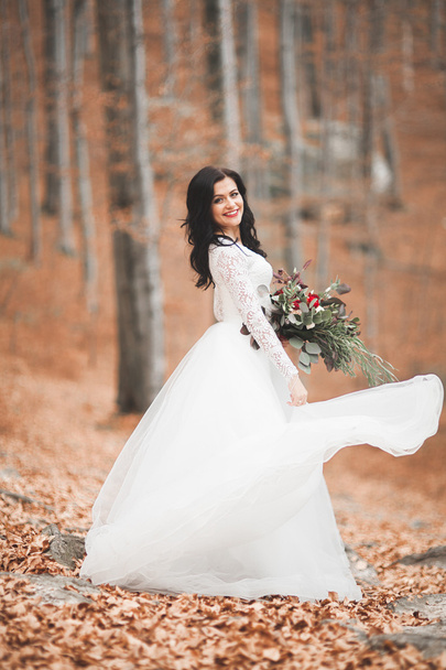 Gorgeous brunette bride in elegant dress holding bouquet  posing near forest and lake - Fotografie, Obrázek