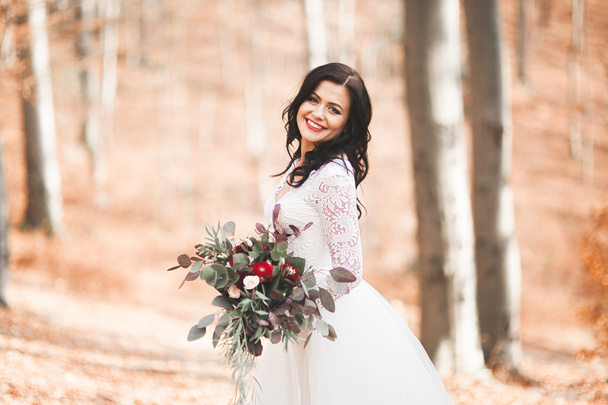 Gorgeous brunette bride in elegant dress holding bouquet  posing near forest and lake - Foto, Imagem