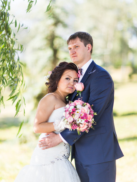 Hochzeitspaar umarmt, die Braut hält einen Blumenstrauß, der Bräutigam umarmt sie - Foto, Bild