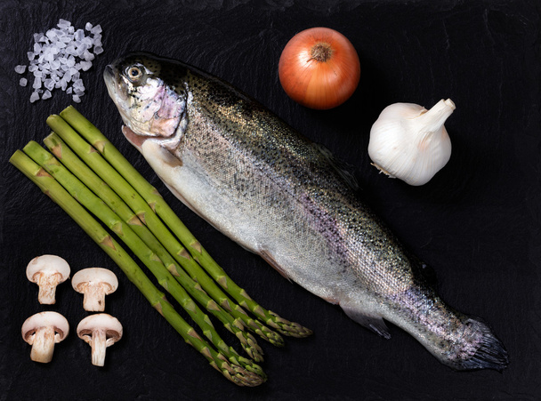 roher ganzer Fisch mit Gemüse und Gewürzen auf Naturschieferstein - Foto, Bild