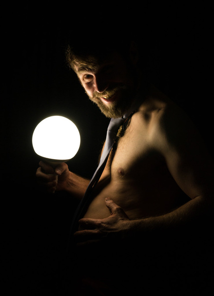 bearded man with a large belly in a tie on a naked body holding a large lamp - Foto, afbeelding