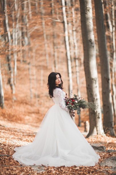 Gorgeous brunette bride in elegant dress holding bouquet  posing near forest and lake - Valokuva, kuva