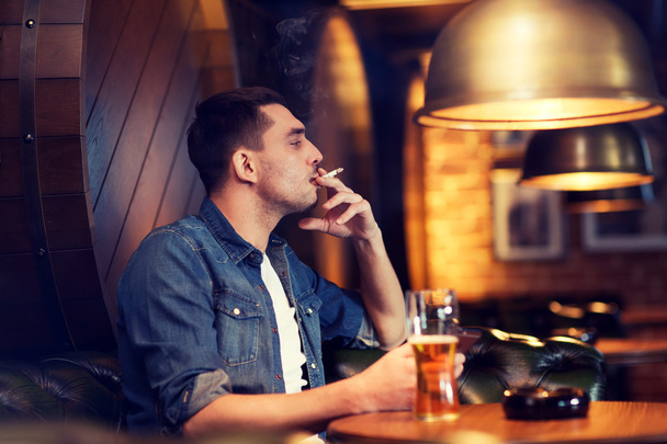man drinking beer and smoking cigarette at bar - Fotoğraf, Görsel