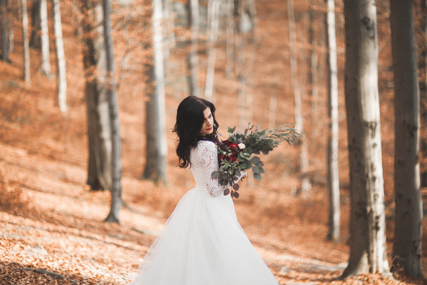 Gorgeous brunette bride in elegant dress holding bouquet  posing near forest and lake - Fotoğraf, Görsel