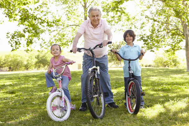 Grandfather With Grandchildren In Park Riding Bikes - Foto, Bild