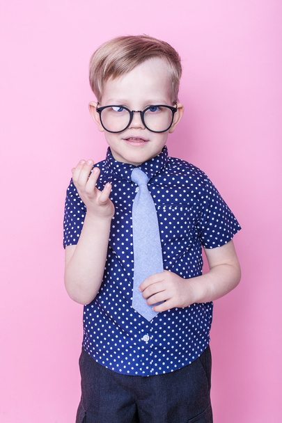 Портрет маленького улыбающегося мальчика в смешных очках и галстуке. В школу. В садик. Мода. Студийный портрет на розовом фоне
 - Фото, изображение