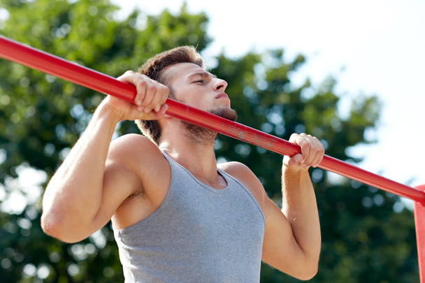 young man exercising on horizontal bar outdoors - Photo, Image