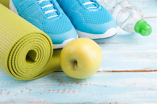 Коврик для йоги, спортивная обувь, яблоко, бутылка воды на голубом деревянном пакете
 - Фото, изображение