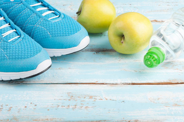 Sport shoes, apples, bottle of water on blue wooden background.  - Photo, Image