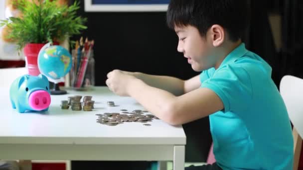 Menino asiático feliz contando moedas do banco porquinho e juntos
 - Filmagem, Vídeo