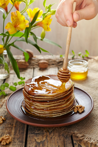 Difundir miel en la pila de panqueques caseros tradicionales con nueces
 - Foto, imagen