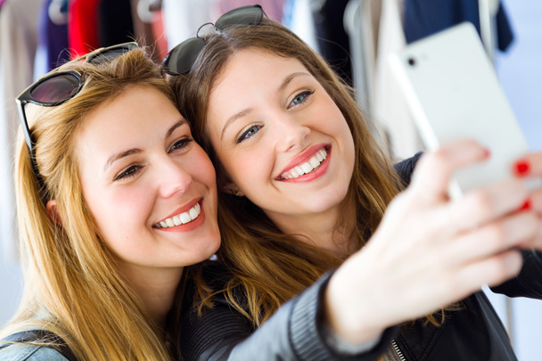 Two beautiful young women using their mobile phone in a clothes  - Foto, Imagem