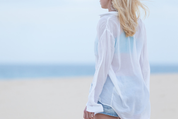 Femme sur la plage de sable en chemise blanche au crépuscule
. - Photo, image