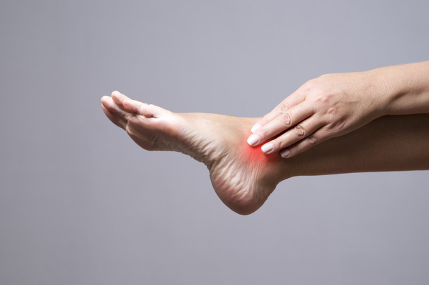 Pain in the foot. Massage of female feet. Pain in the human body on a gray background - Fotó, kép