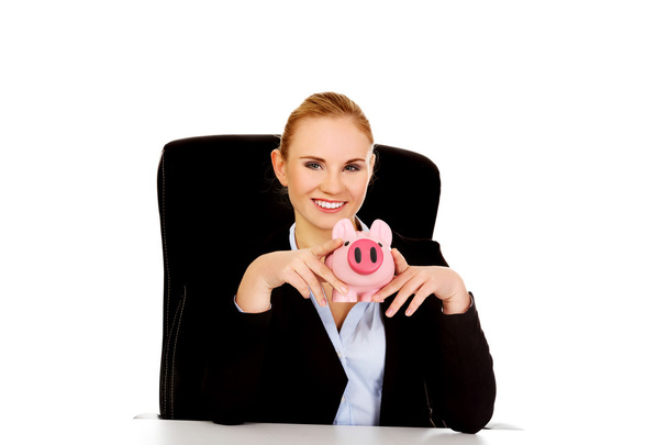 Happy business woman with a piggybank behind the desk - Fotoğraf, Görsel
