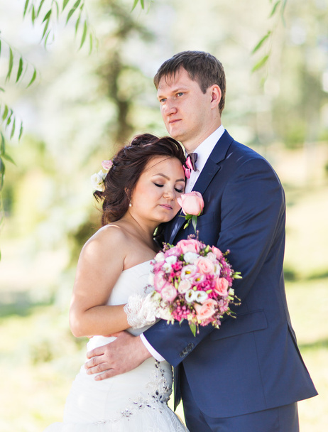 γαμήλιο ζεύγος αγκάλιασμα, η νύφη που κατέχουν ένα μπουκέτο λουλούδια, γαμπρός αγκαλιάζοντάς την - Φωτογραφία, εικόνα