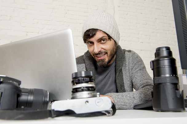 ελκυστικός φωτογράφος τύπου που εργάζεται με φορητό υπολογιστή και γραφείο γεμάτο φωτογραφικό γρανάζι - Φωτογραφία, εικόνα