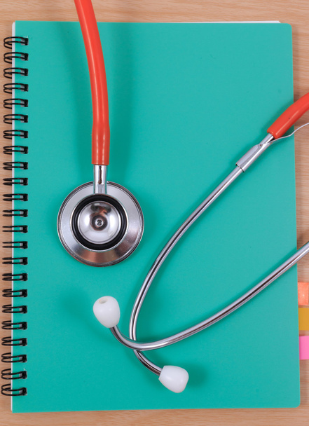 Red stethoscope lying on a thin green book. - Photo, Image