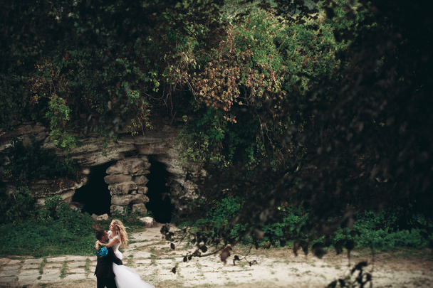 Luxury wedding couple hugging and kissing on the background gorgeous plants, cave near ancient castle - Фото, изображение