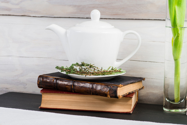 White teapot with green leaves herbal tea and old books - Fotó, kép