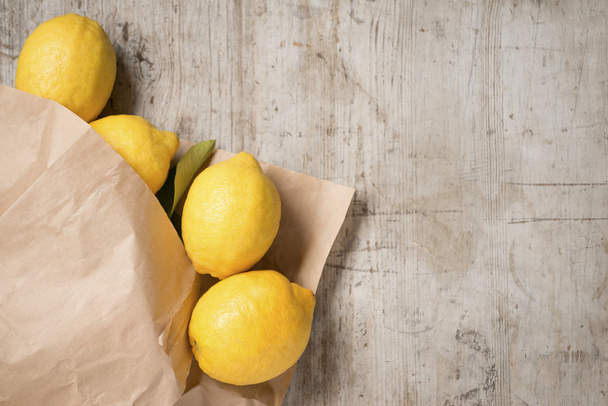 Лимоны в бумажном пакете на деревянном фоне
  - Фото, изображение