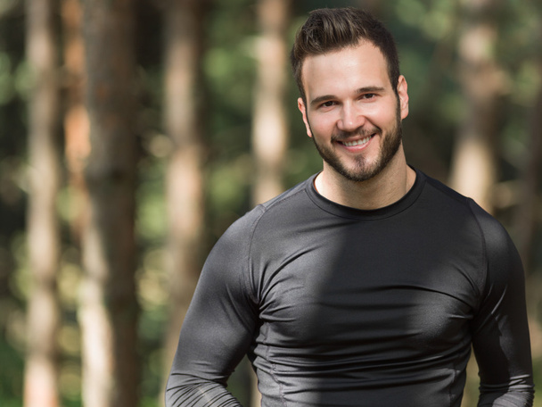 Smiling handsome muscular young man standing outdoors in a woode - Foto, Imagem