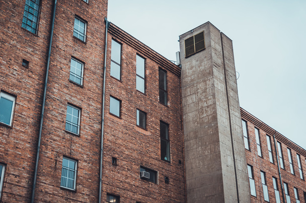Low angle view on rear section of old brick building with concrete elevator shaft on exterior wall - Valokuva, kuva