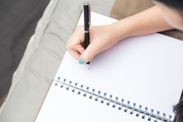 Γυναίκες χέρι γράψιμο σε κενό σημειωματάριο με στυλό στο κρεβάτι. - Φωτογραφία, εικόνα
