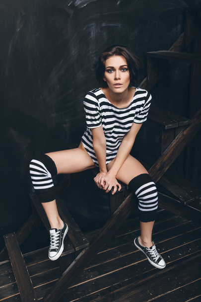 Girl in striped bodysuit against black wall - Fotó, kép