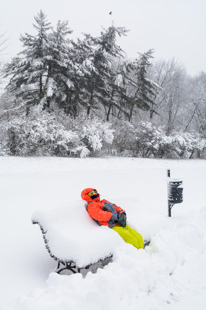 Мальчик лежит на скамейке со снегом. Вертикальный вид с ребенком i
 - Фото, изображение